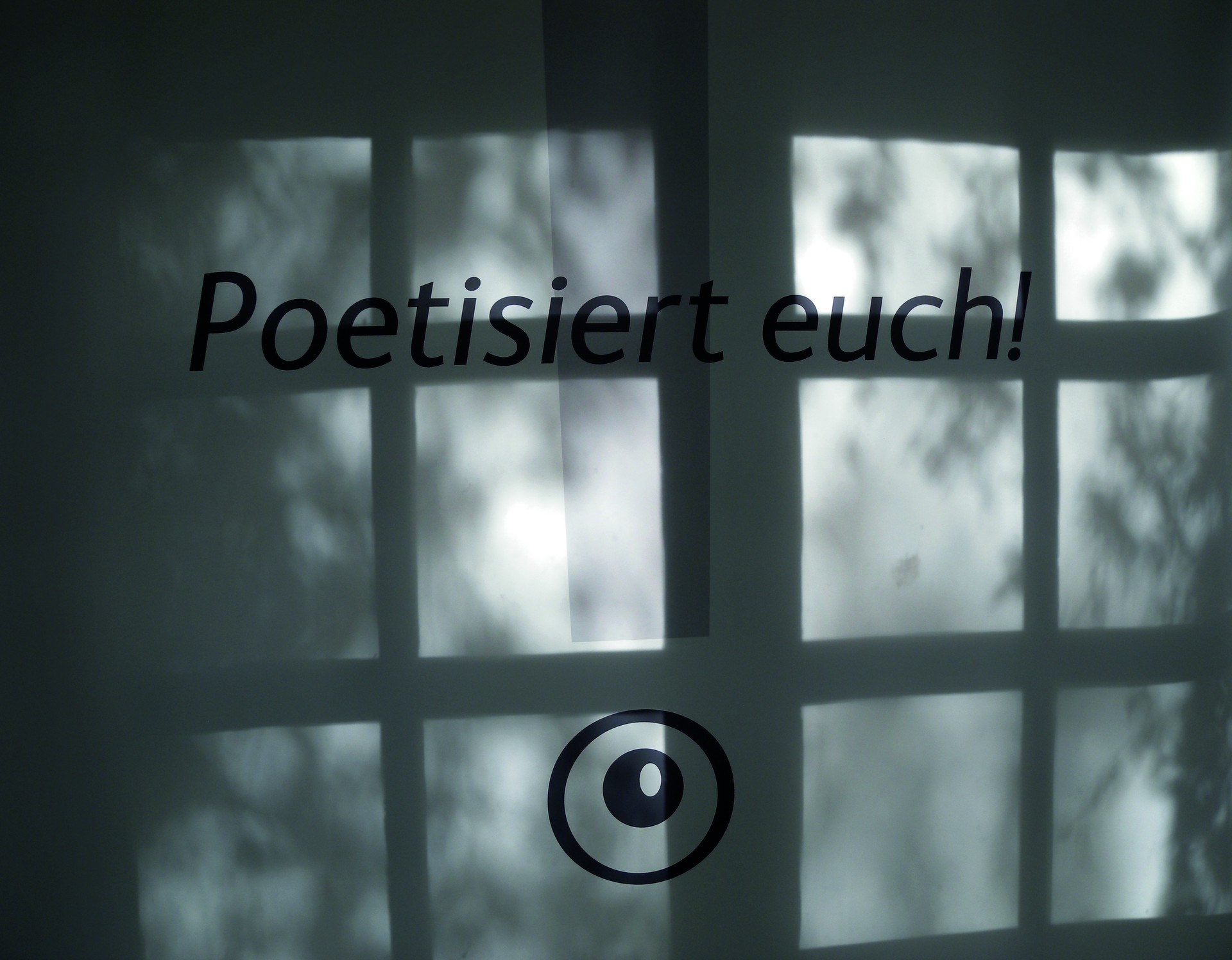 Wandbeschriftung "Poetisiert euch!", darüber Schattenwurf eines Sprossenfensters